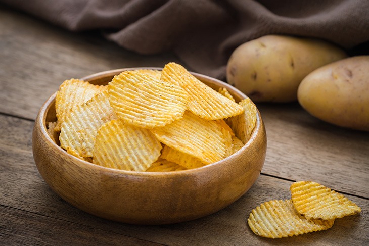 Potato chips in bowl and fresh potato